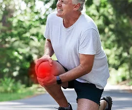 Grey-haired man kneeling on a path with one hand on his knee