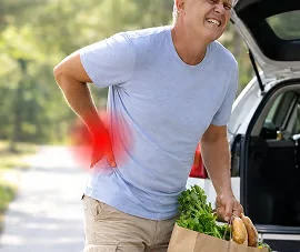 Man carrying a grocery bag with one hand pressed to his lower back