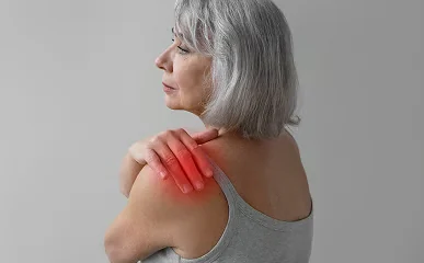 Woman in a grey tank top reaching for her shoulder